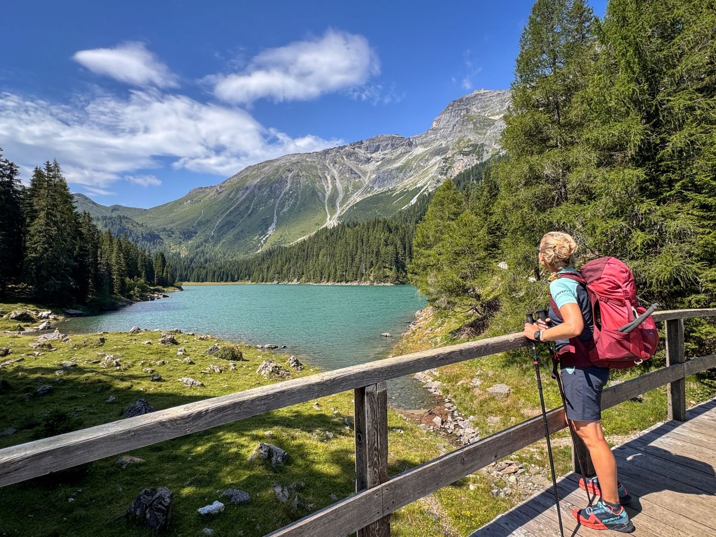 Hiker on a wooden bridge overlooking the turquoise alpine lake, a scenic highlight of the Garmisch to Sterzing trekking route - supplied by Eurohike
