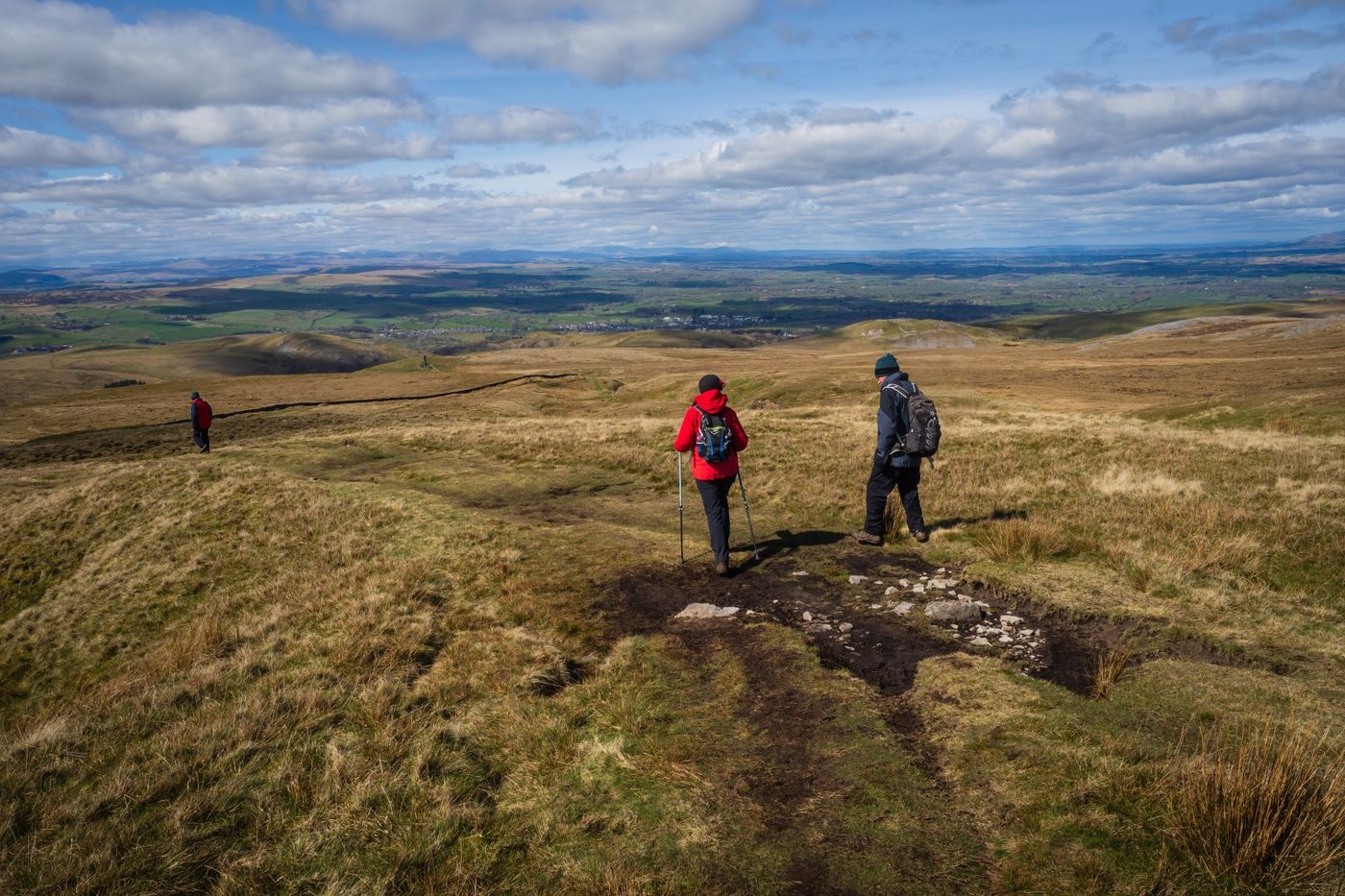 Hikers walking along a high, grassy trail on Hartley Fell with the views of Eden Valley in Kirkby Stephen