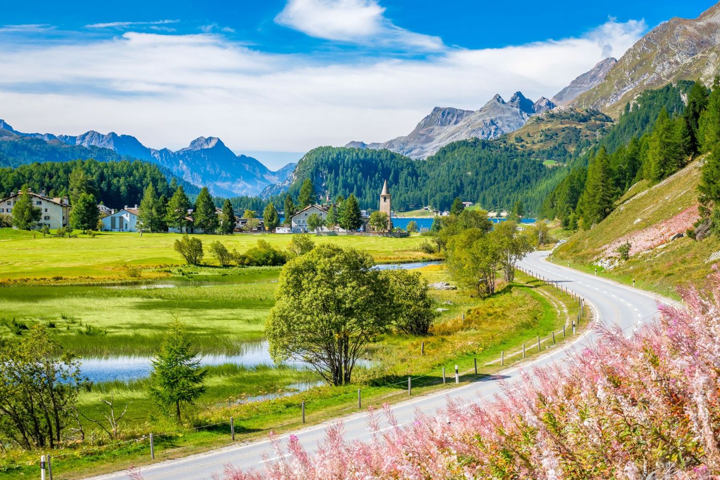 Paved road winding toward the historic church tower of Sils Baselgia and Lake Sils